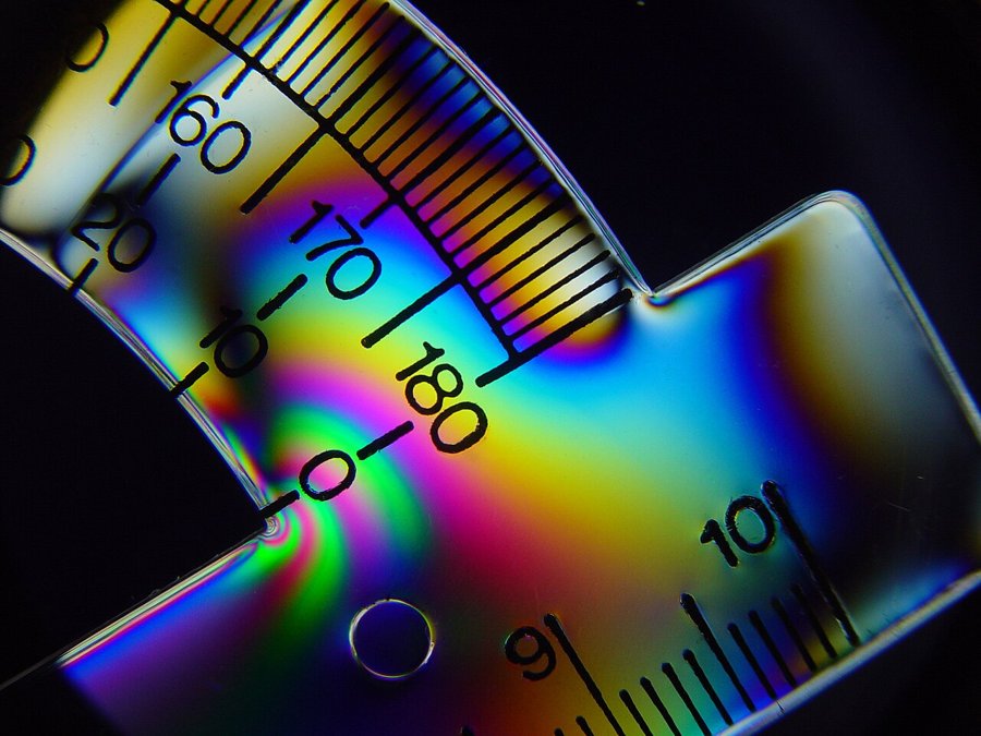 A plastic protractor between two polarizers, showing coloured stress bands